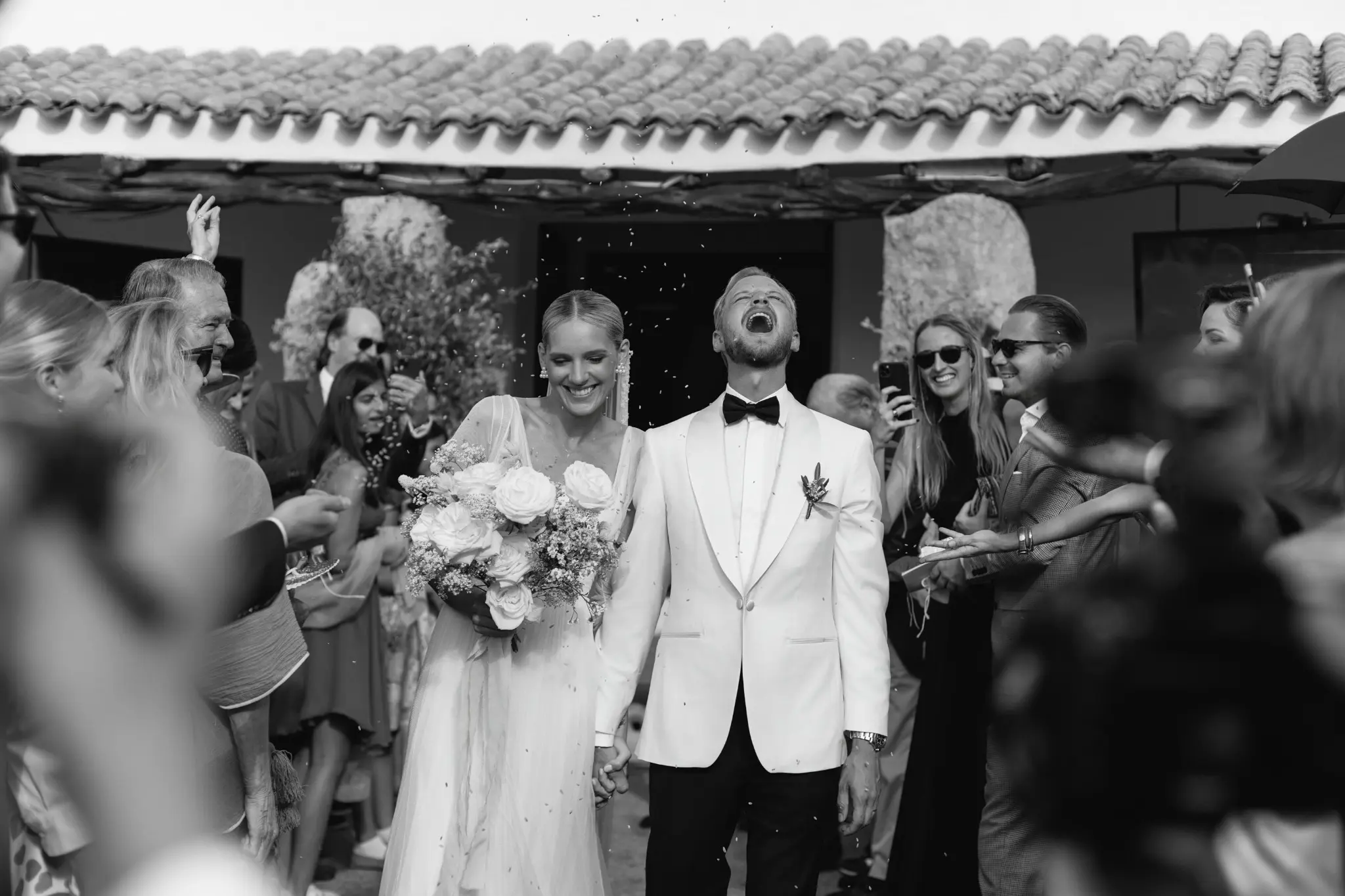 Laura and Leo leaving their wedding ceremony surrounded by guests in Sardinia