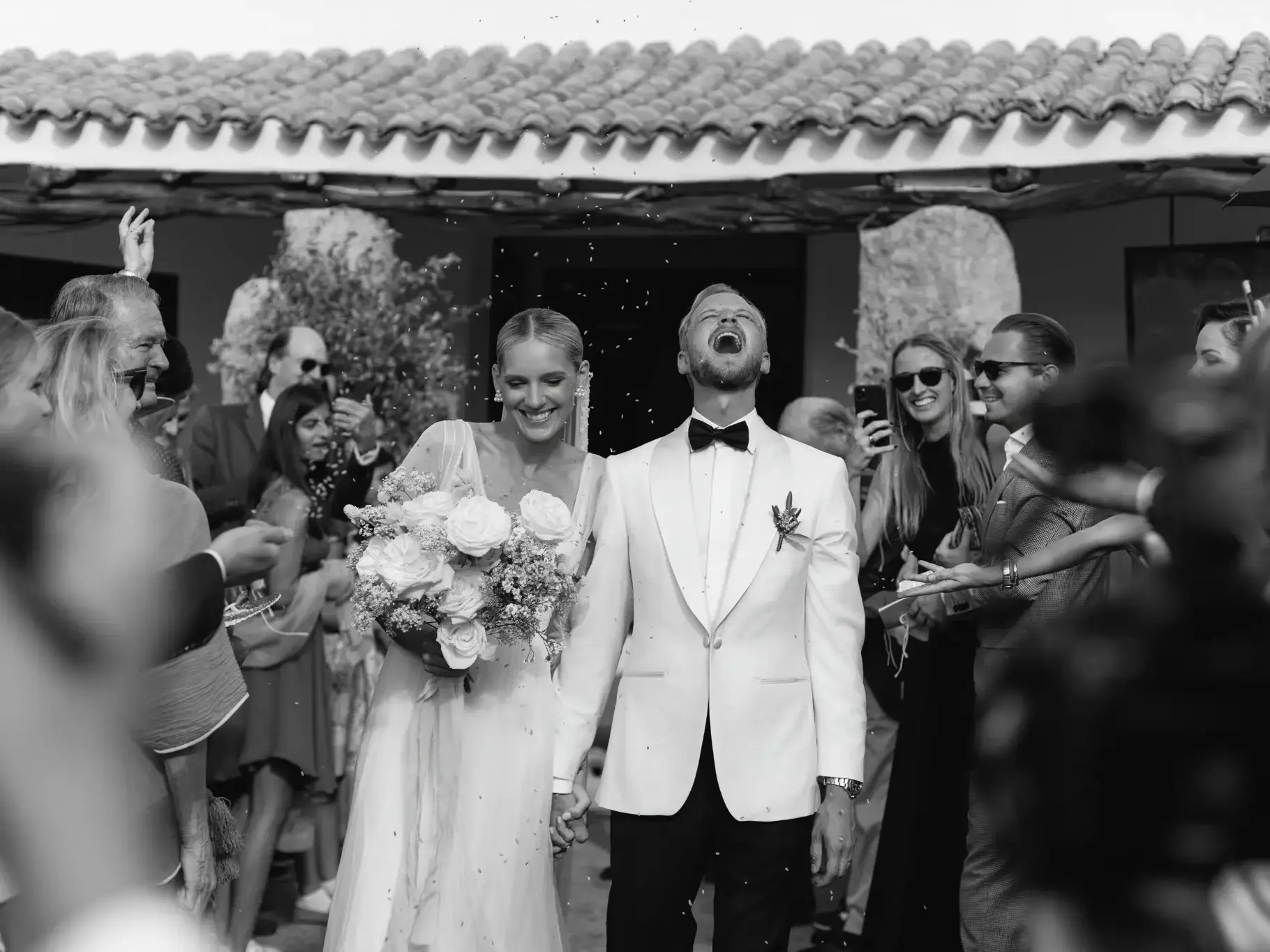 Laura and Leo leaving their wedding ceremony surrounded by guests in Sardinia
